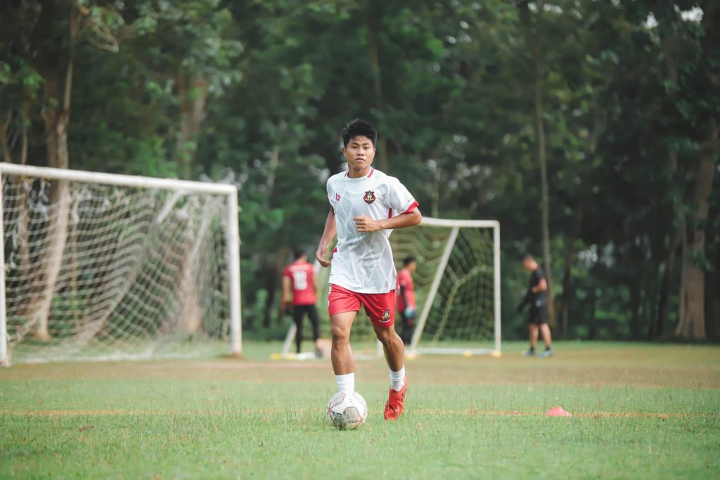 Teen soccer player practicing on a lush outdoor field, focused on training.